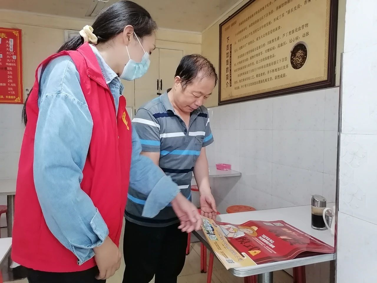 志愿者向餐饮店经营者发放文明餐桌宣传彩页